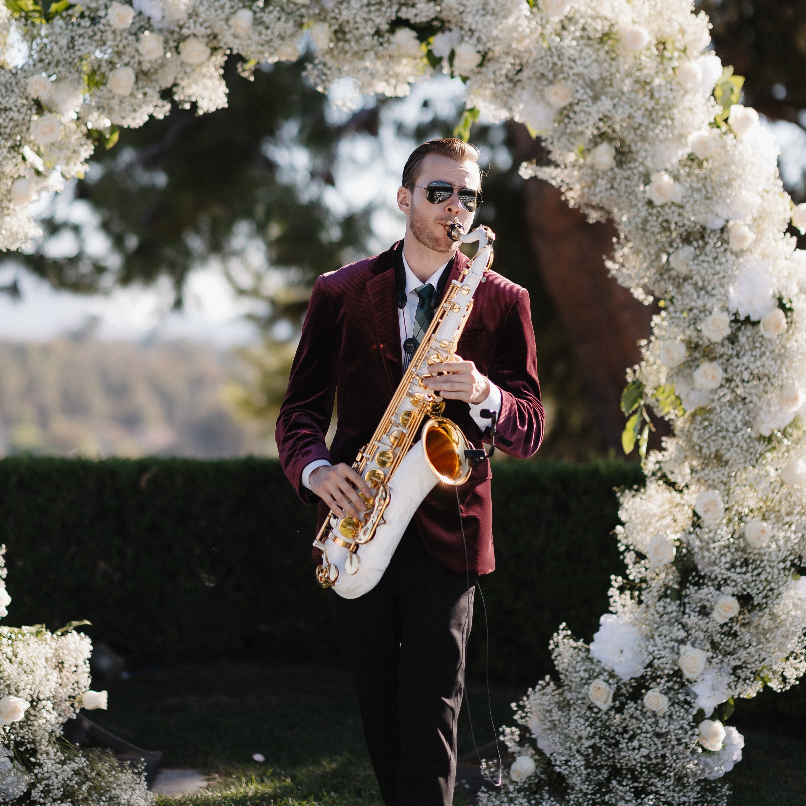 Saxophonist walking down the aisle, playing a white saxophone.